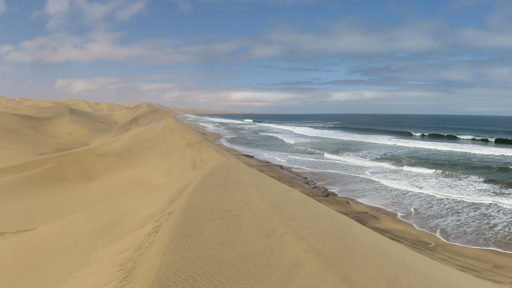 Sandwich Harbour giant desert sand dunes plunging into the Atlantic ocean breakers in Namibia.