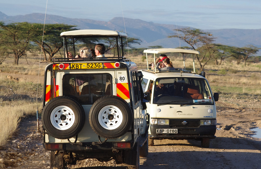 Customized four-wheel-drive safari Land Cruiser with open pop-up roof traversing savannah tracks in Kenya.