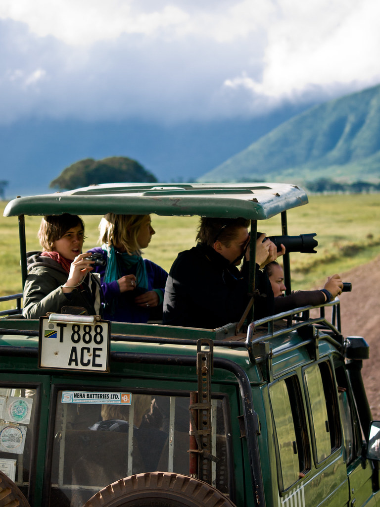 Professional telephoto camera lens mounted securely on a beanbag along the sidebar of an open safari vehicle.